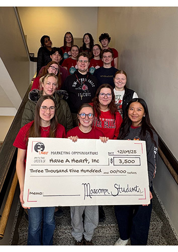 Students wearing mostly red and black pose with an oversized donation check