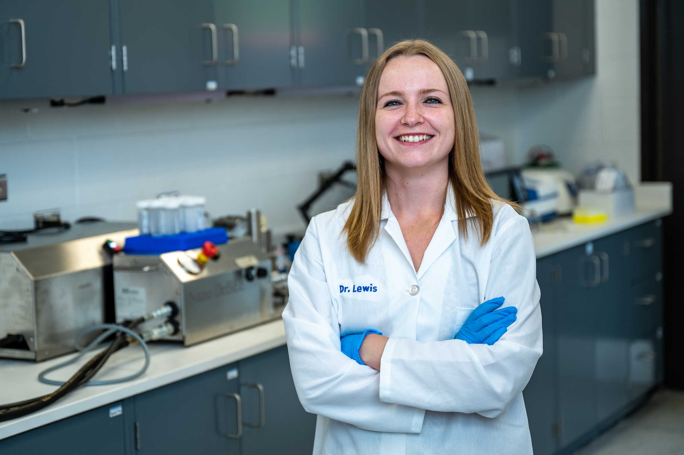 Middle-aged white woman with shoulder-length blonde hair wearing a lab coat stands in a dairy laboratory