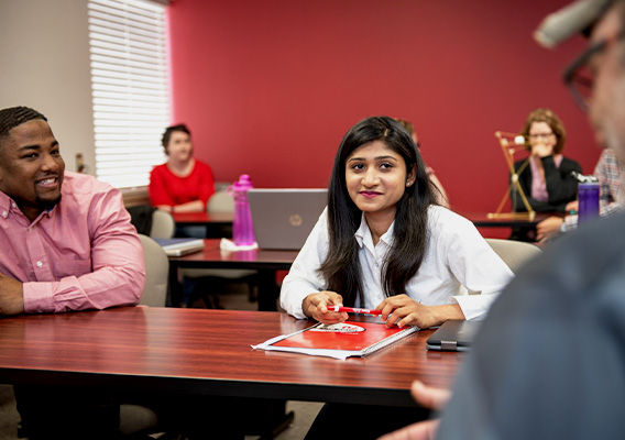 Two Graduate students listen to another student speak during class