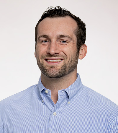 Headshot of Grant Erickson, a young man with black curly hair and stubble wearing a light blue button up shirt