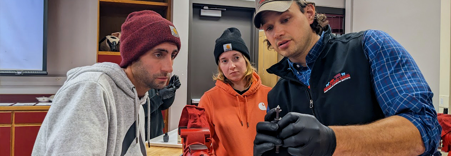 A professor shows a drill bit to two students in a lab classroom