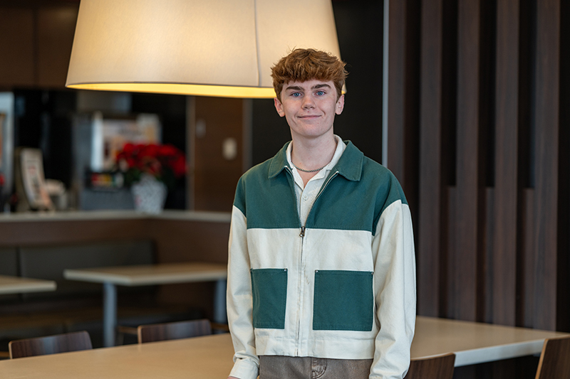 a white male wearing a green and white jacket stands in front of a table and chairs.