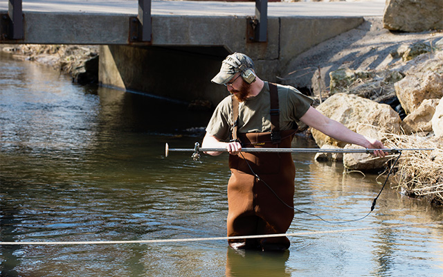 Student stands in the Kinnickinnic River testing the water