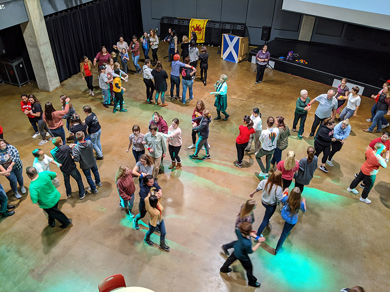 An aerial view of dozens of people on a dance floor in small clusters. Green lights are visible on the dance floor.