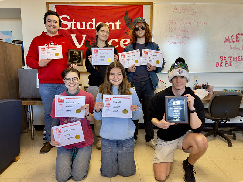 two rows of students holding award certificates stand in front of a banner that says "Student Voice"