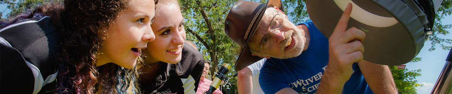 Two students look into a telescope at a partial solar eclipse