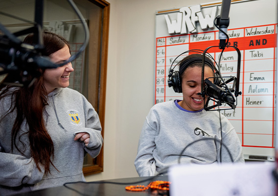 Two female students sit in the WRFW radio station with microphones