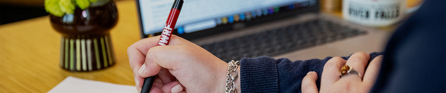 A person sits with an open laptop taking notes in a notebook
