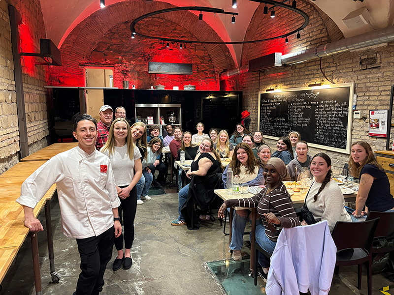 a group of 20 or so people stand and sit inside an Italian restaurant