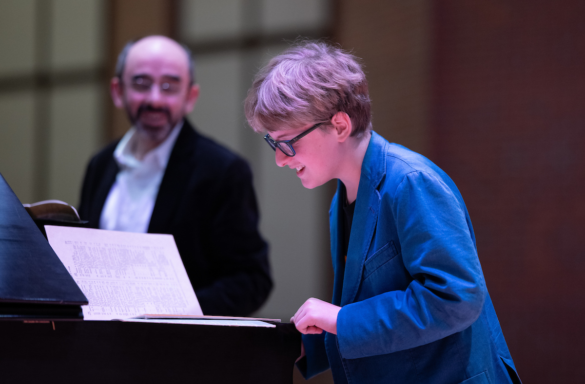 student learning piano music while guest artist overlooks and discusses