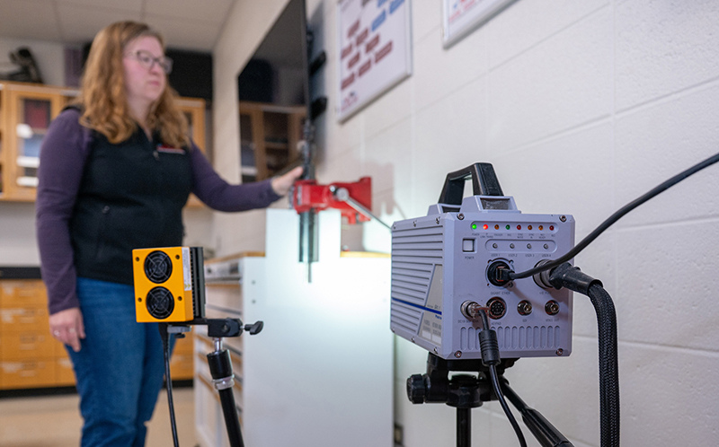 a woman looks over a high speed camera and captive bolt tool