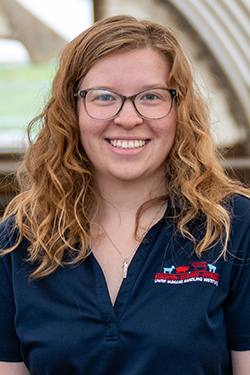 Karly Anderson headshot. A white woman with strawberry blonde curly hair is wearing glasses and a polo that says "UWRF Humane Handling Institute"
