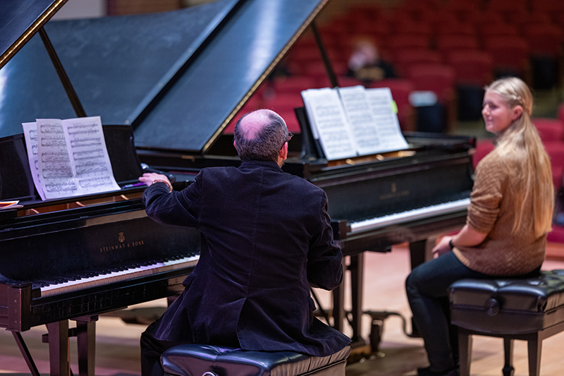 two people sit at pianos with their backs to the camera