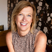 Kim Peterson headshot. A woman with shoulder length dirty blonde hair, wearing a sleeveless polka dotted top, smiles at the camera.