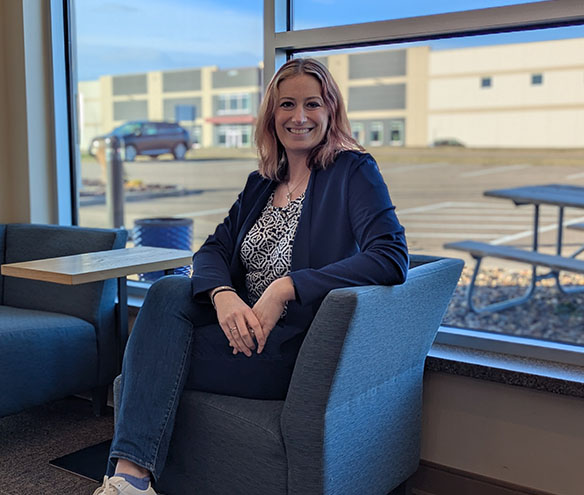 a woman wearing a navy sweater, printed blouse and blue jeans sits on a blue chair