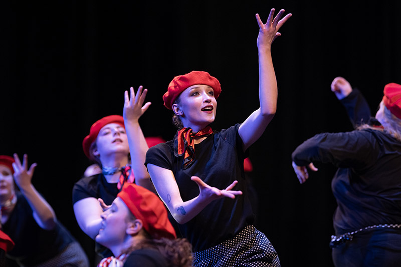 dancers wearing black shirts, red scarves and red berets perform on stage