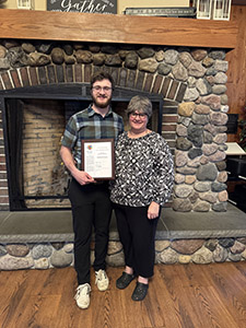 two people standing in front of a fireplace, one male holding a plaque and a female next to him.