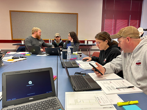 group of men and women sit at table working on computers