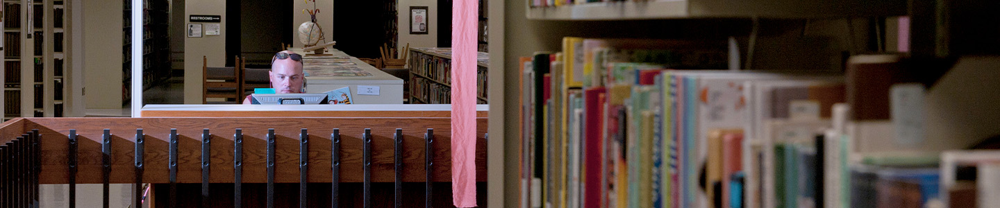 A student sitting in the library among rows of books