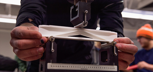 A student places a section of a miniature bridge under a hydraulic press during a test