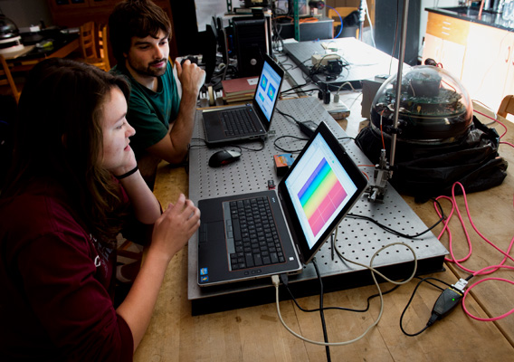 Two students stare at a laptop waiting for data on their experiment