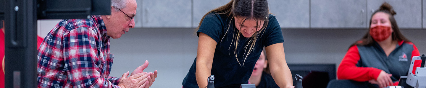 Health and Human Performance professor encourages student on a stationary bike