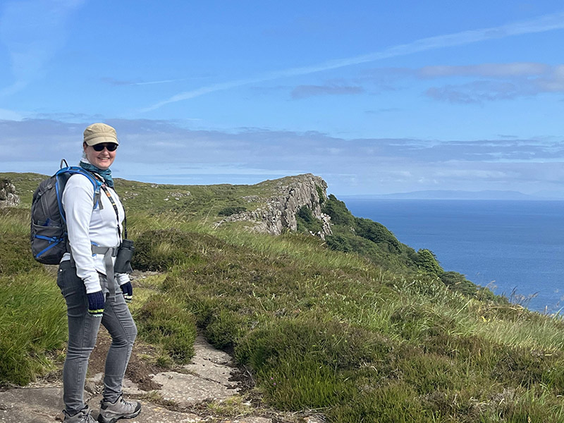 a hiker wearing a hat and backpack stands in the foreground overlooking a grass covered cliff