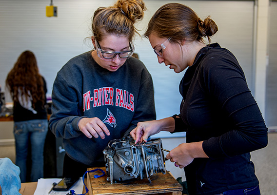 Two students examine a broken small engine during class
