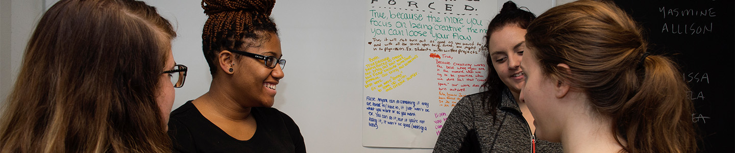 Four Sociology students review notes in front of a whiteboard