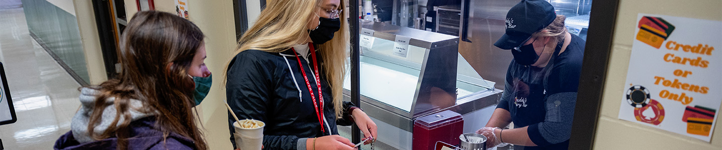 A student prepares an ice cream cone at Freddy's Dairy Bar for two other students