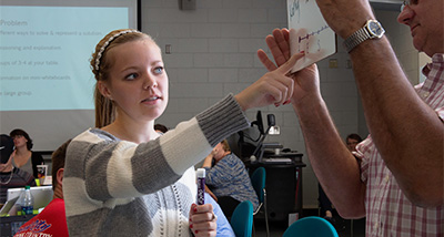 Student points to a handheld whiteboard with writing on it