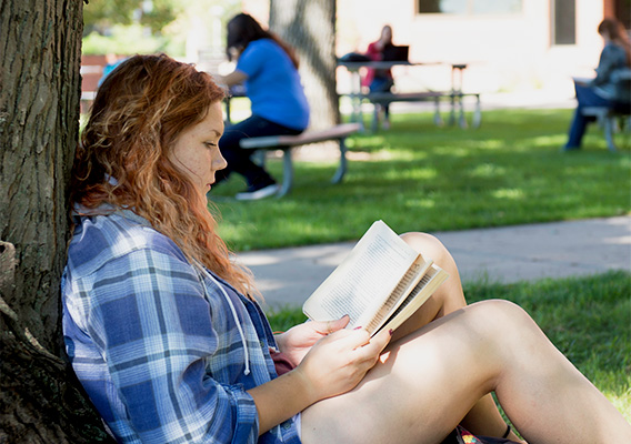 Student reads a book underneath a tree 