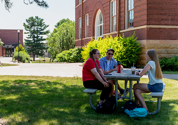 Three students sitting at a picnic table talking