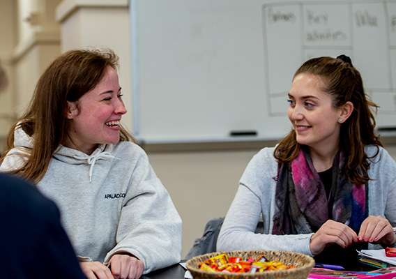 Two students smile and talk during class