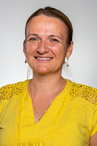 Sylvia Kehoe headshot. A woman with short brown hair wears a yellow top and long earrings.