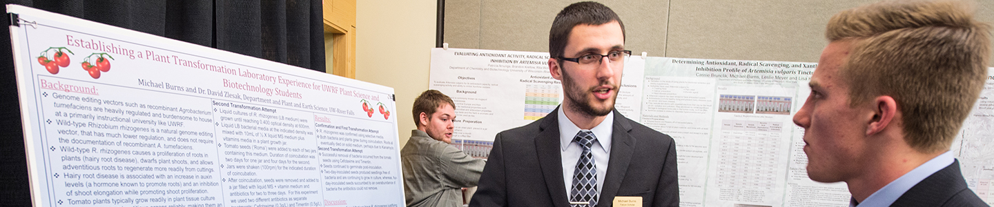 One student explains his research poster to a fellow student at the research showcase