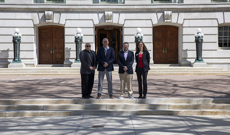Four people in business dress stand outside the Wisconsin Capitol building