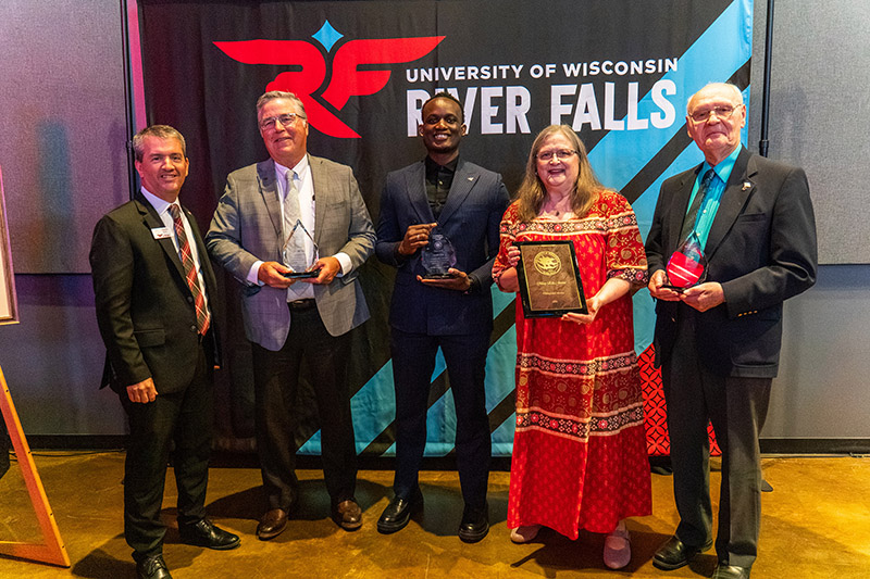 Five people dressed in business attire hold plaques
