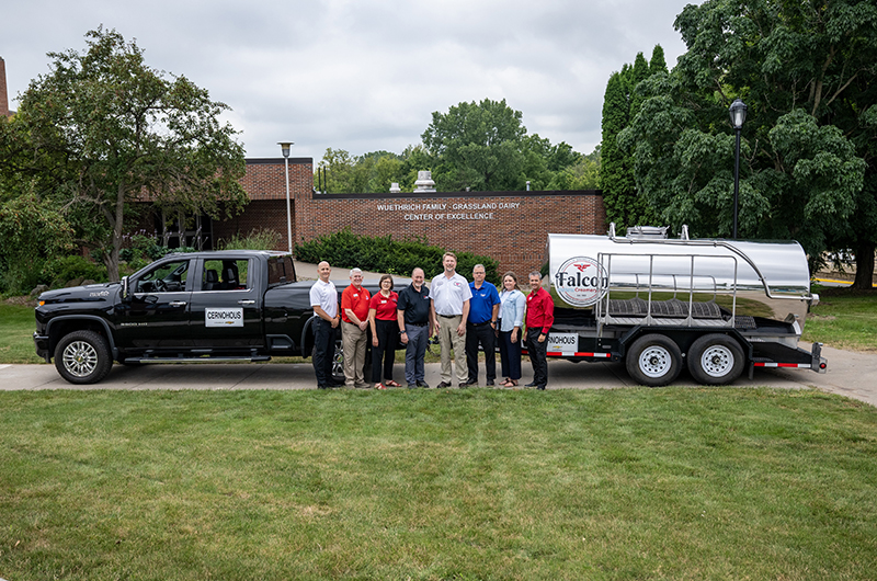people stand in front of a truck and milk hauler