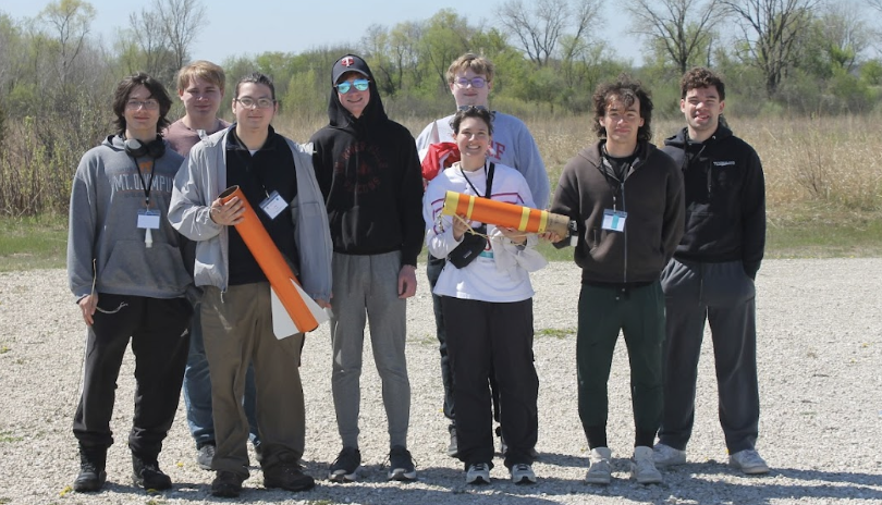 A group of eight people stand together while holding a rocket they built