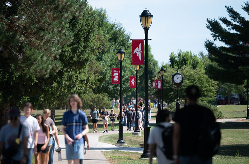 Students walk through campus. Flags with the UWRF logo are on the lampposts.