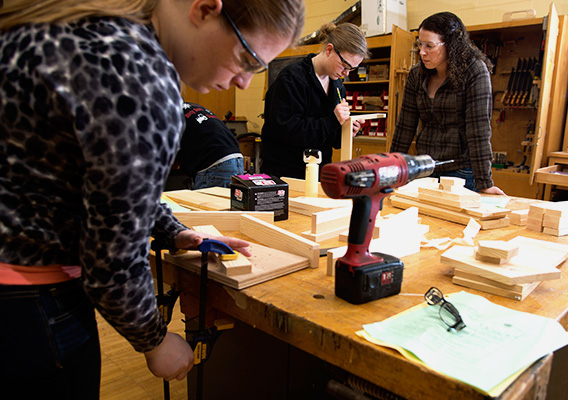 Three graduate students work on their projects in the campus wood shop