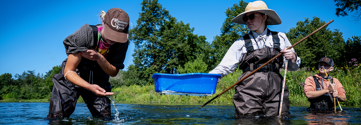 Two female student stand in the Kinnickinnic River taking samples for the Freshwater Collaborative project