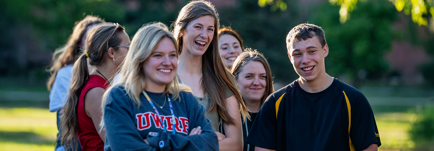 A group of students that are outside, listen to a speaker during the orientation
