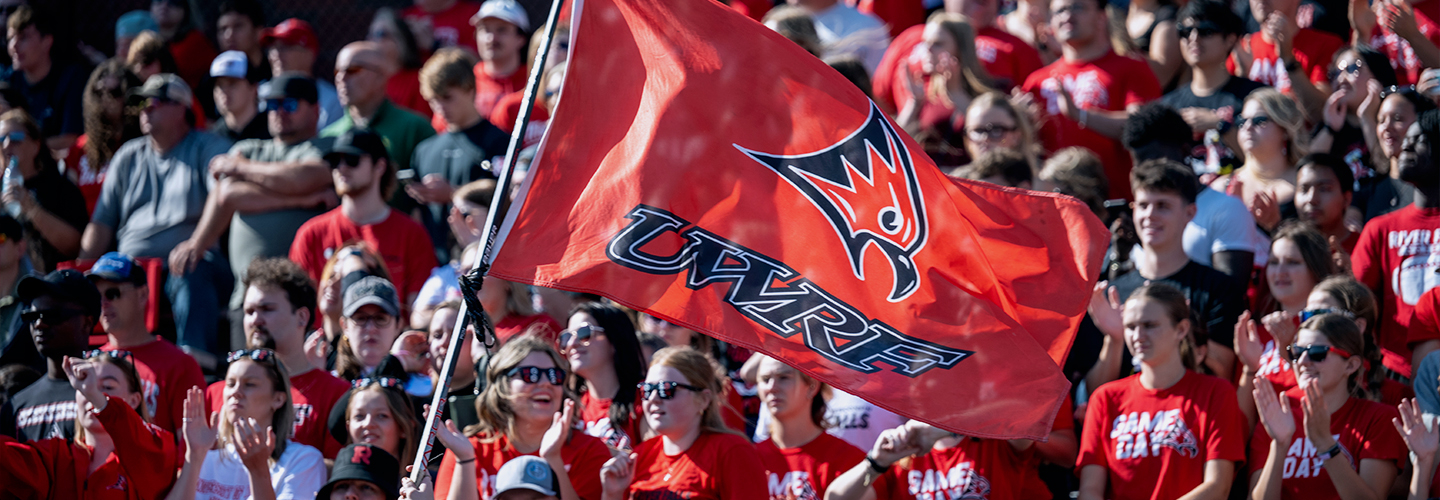 A crowd of students at a UWRF Football game with a UWRF flag being waved by one student